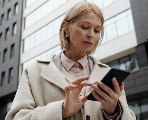 A lady holding a cellphone between some building representing business people